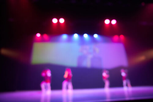 A colored blurry background of a dance festival from a group of little girls. Bright stage lighting. Silhouettes of little dancers. High quality photo