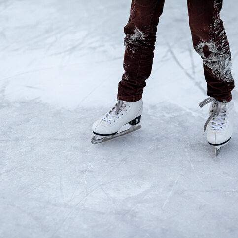 A pair of white figure skates with laces on frozen ice close-up. A man is skating. Ice skating or playing hockey in winter. ice and legs and copy space over ice background with marks from skating